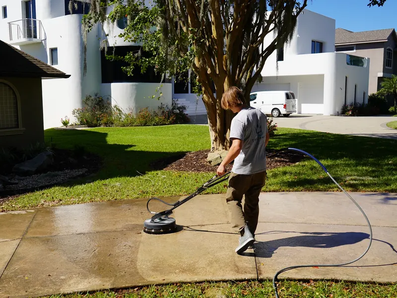 Trident technician using a surface cleaner on a concrete driveway in front of a home