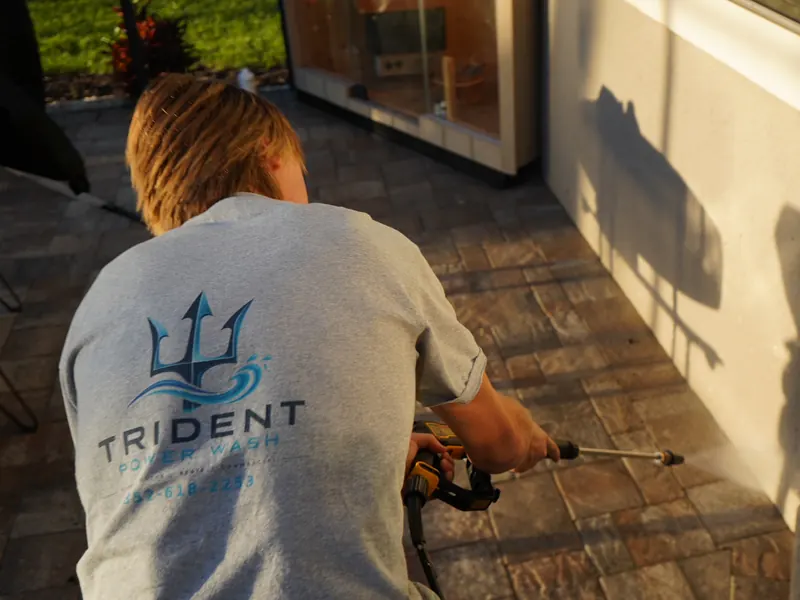 Trident technician in a Trident shirt pressure washing pavers beside a home