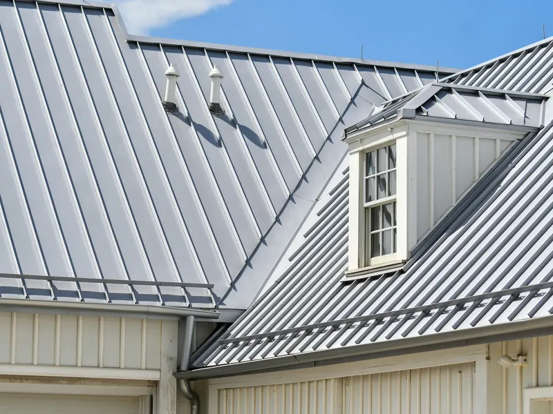 Clean standing-seam metal roof with a dormer window under a blue sky